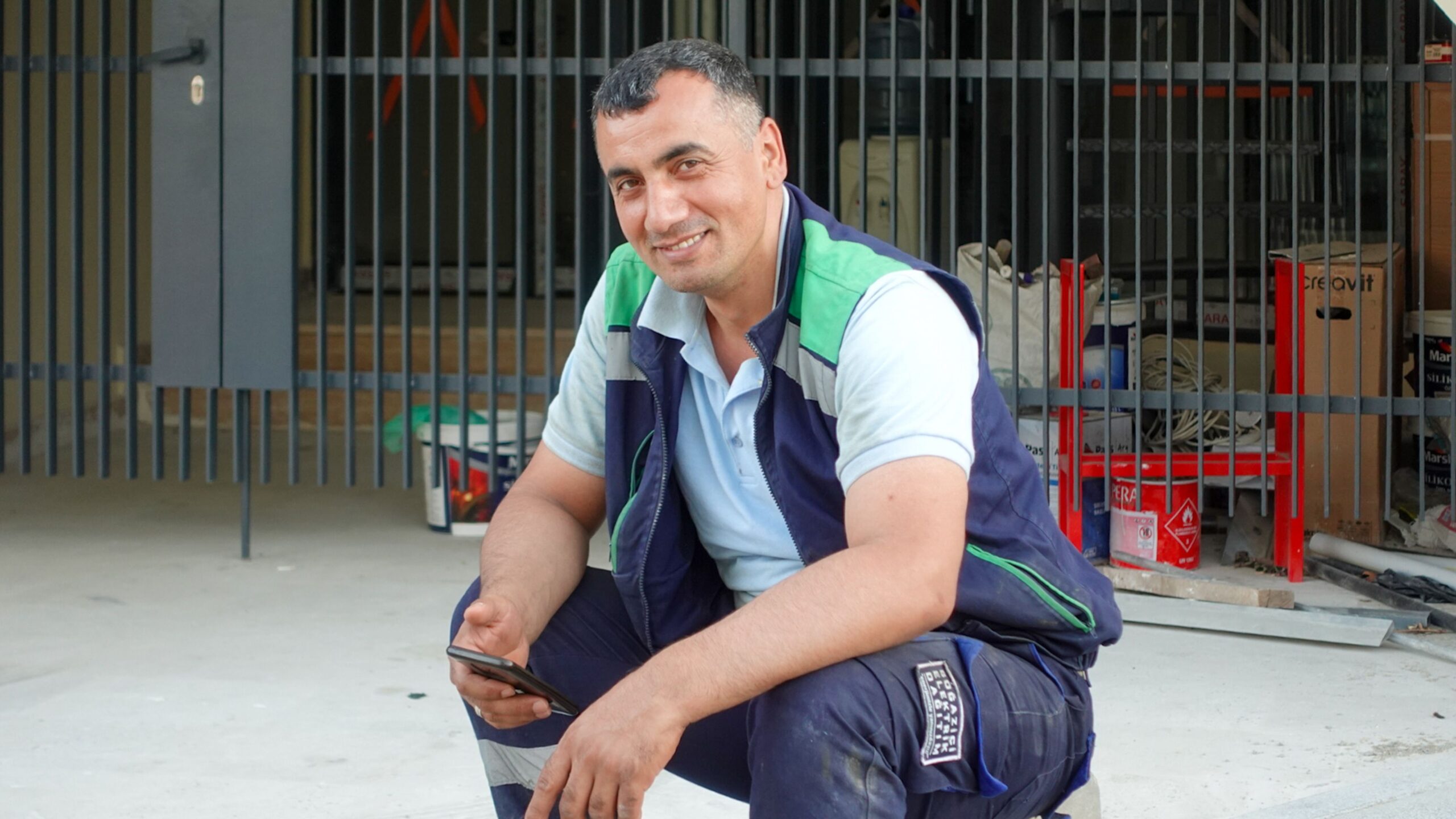 Happy construction worker taking a break using smartphone outside a building site.